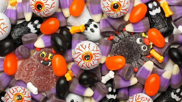 Close up image of purple, orange, black and white candies in various Halloween-inspired shapes including ghost, eyeballss, bones and bats. 