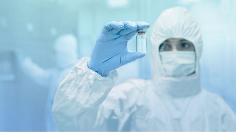 Scientist in protective gear holding vial, representing advanced cell therapy manufacturing with active-release magnetic bead technology.
