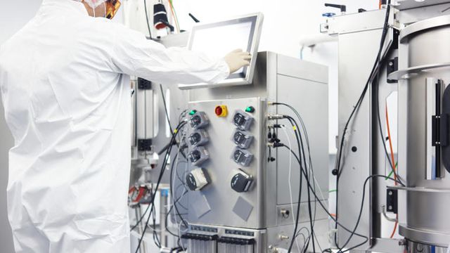 Scientist in protective suit operating a bioreactor system using a touchscreen in a cleanroom lab 