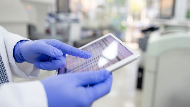 Gloved scientist using a tablet to access LIMS data in a modern laboratory setting. 
