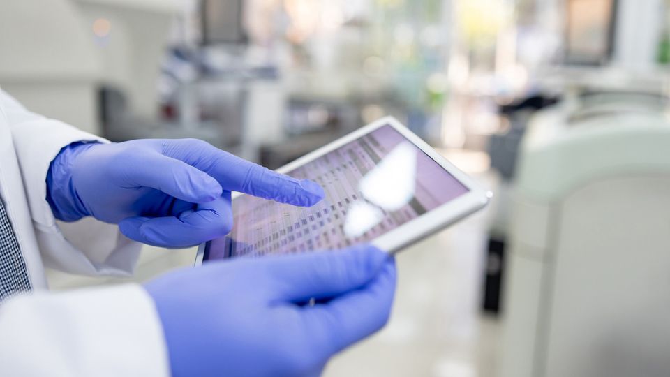 Gloved scientist using a tablet to access LIMS data in a modern laboratory setting.
