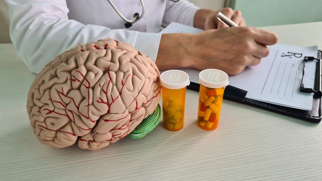 A doctor prescribing medication with a bottle of pills and model of a human brain on the desk, representing OCD treatments. 