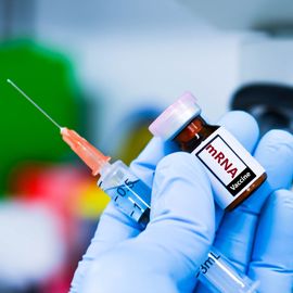 Syringe and vial of mRNA vaccine held in a gloved hand. 