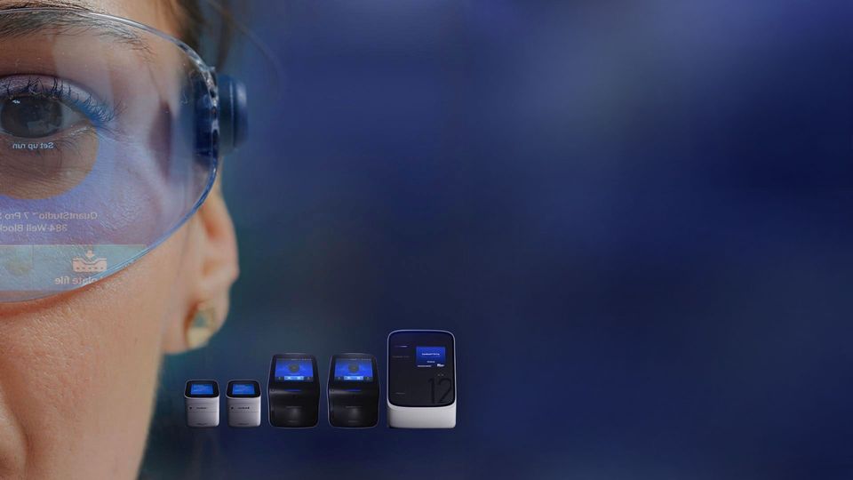 Close-up of a scientist wearing protective goggles with a reflection of lab equipment, alongside a set of PCR machines on a dark blue background